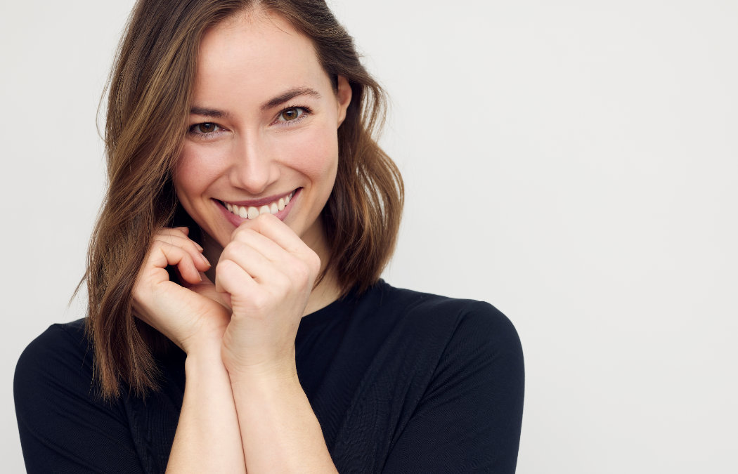 Woman with shoulder-length hair smiling and holding her hands near her face, wearing a black top against a plain background. Atlanta, GA