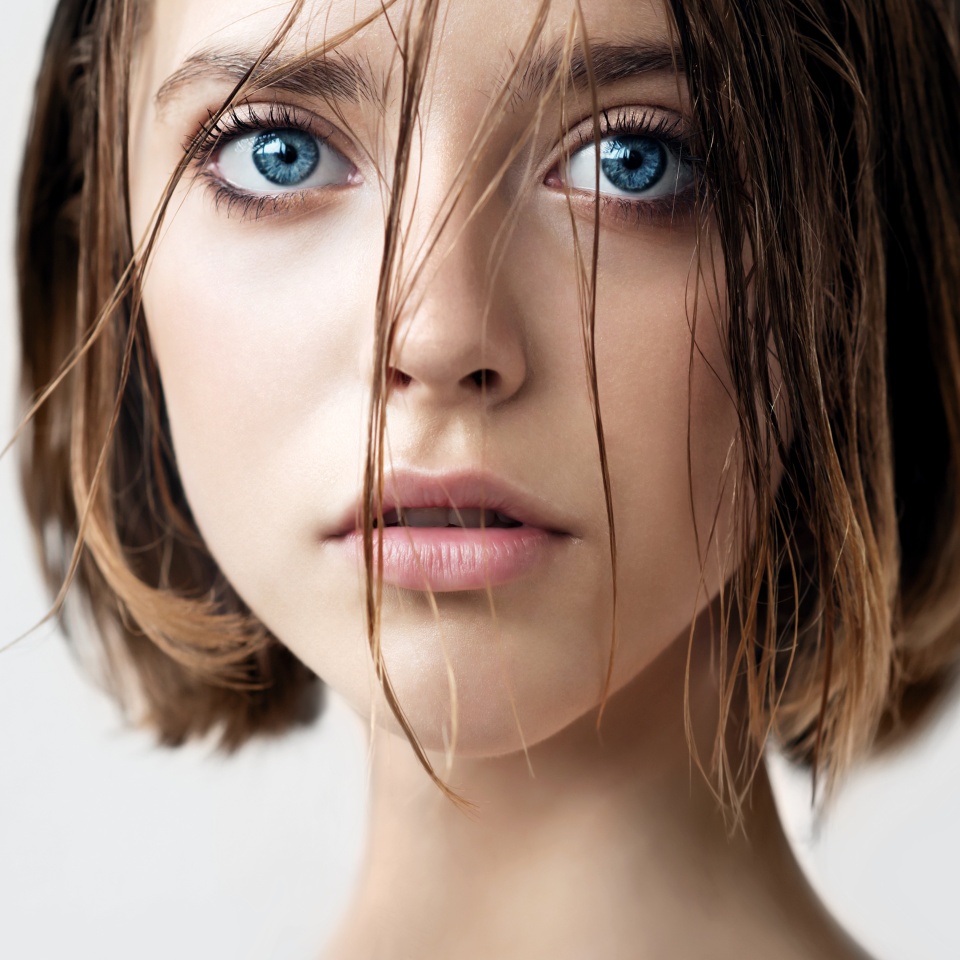 Beautiful young woman with clean perfect skin and wet hair. Portrait of beauty model with natural nude makeup moisturizing her skin. Spa, skincare and wellness. Close up, background, copy space.