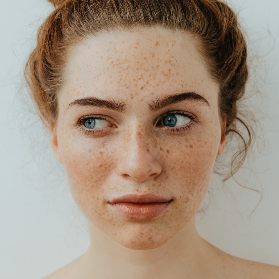 Calm and pretty. Close-up. Beautiful blue eyed girl with freckles is looking away, on a white background