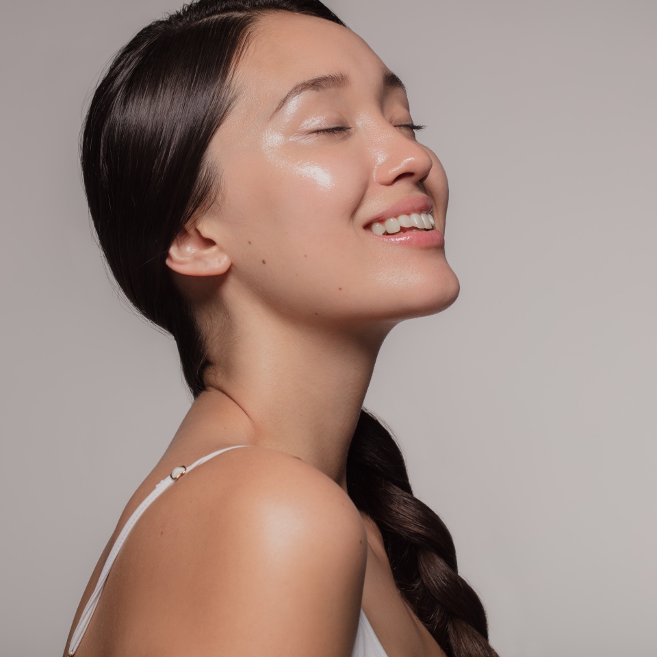 Asian woman with beautiful and healthy skin on beige background. Girl smiling with her eyes closed.