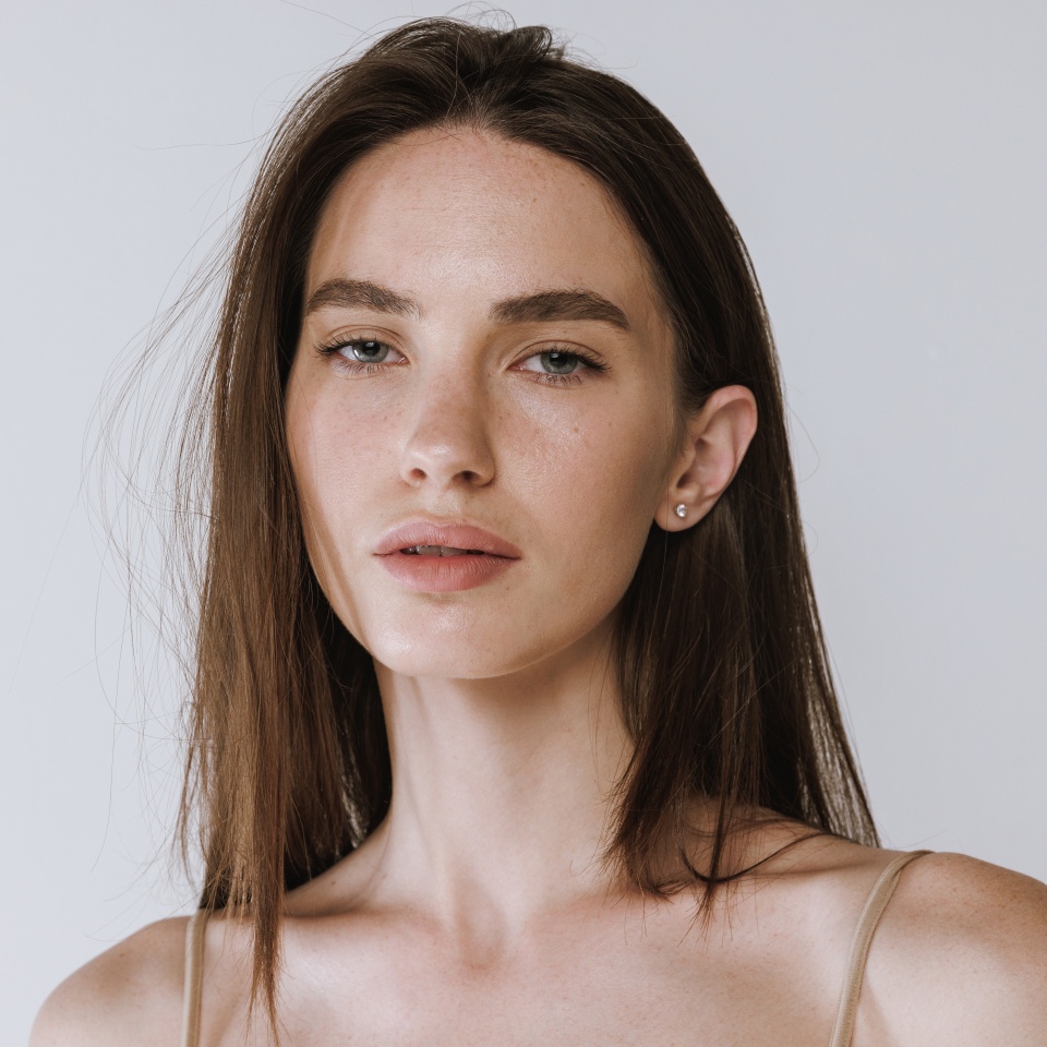 Portrait of tender young girl with beautiful grey eyes and nude makeup posing, looking at camera isolated over gray studio background. Concept of beauty, body and skin care, health, spa, cosmetics, ad