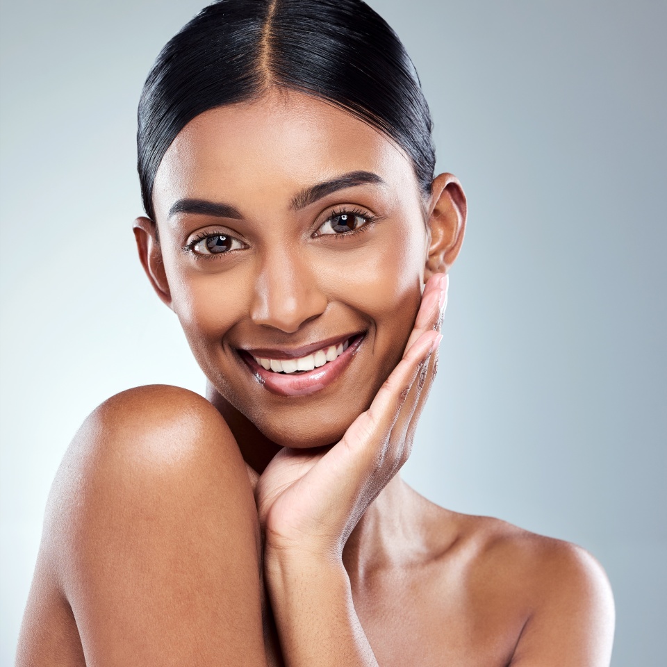 Smile, portrait and Indian woman beauty or model with skincare cosmetic isolated in a studio white background. Clean, natural and female person hand on face happy for self love, care or dermatology