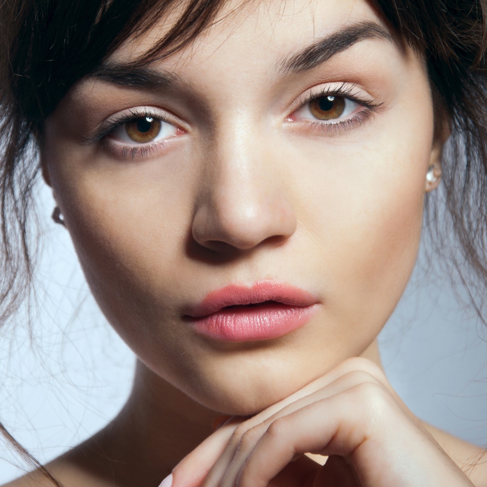 Pretty young woman with natural makeup and perfect skin looking at camera, lips half open. In studio