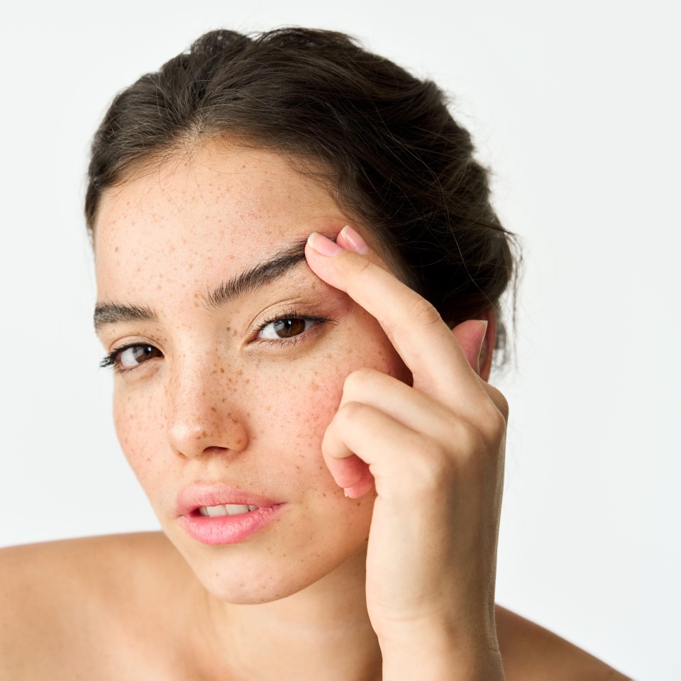 Young adult Latin woman, cool brunette gen z girl with freckles on face looking at camera lifting eyebrow isolated on white background. Beauty aesthetic portrait. Skincare, eye surgery and cosmetic ad