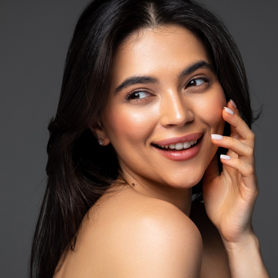 Beautiful young woman with clean perfect skin. Portrait of beauty model with natural nude make up and touching her face. Spa, skincare and wellness. Close up, white background, copyspace