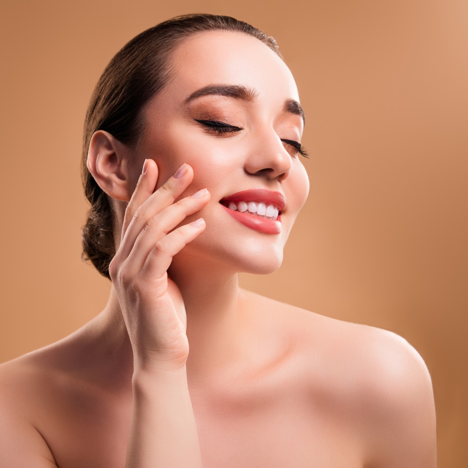 Lovely pretty girl enjoy touch her flawless face skin after moisturizing mask isolated on beige color background