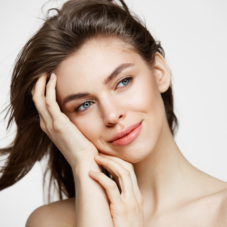 Beautiful naked young girl with perfect clean skin smiling touching hair over white wall. Facial treatment.