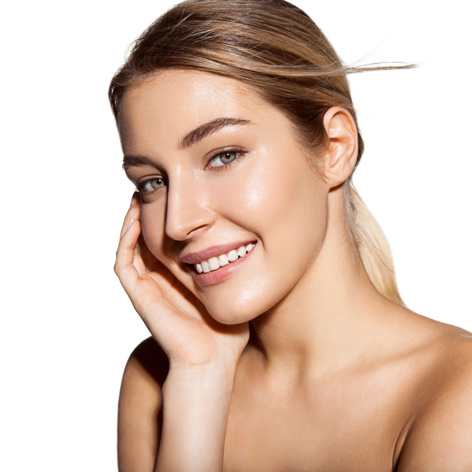 Fashion shiny highlighter on skin of young beautiful model. Happy smiling young woman portrait isolated on white. Blonde model with fresh daily makeup.